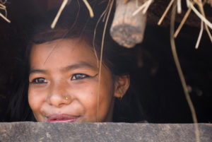 Junges Mädchen in Nepal lächelt durch Öffnung in Hütte