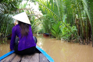 Vietnam. Frau auf Holzboot schippert über braunen Fluss